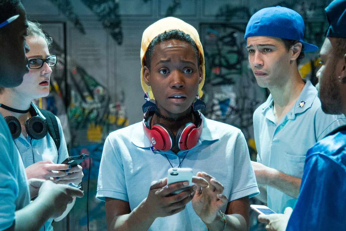 a young black person wearing a blue polo shirt, yellow cap, and red headphones looking at their phone