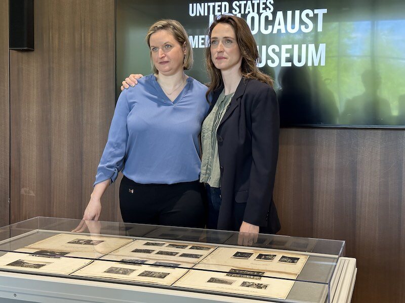 Two women stand behind display case containing photographs