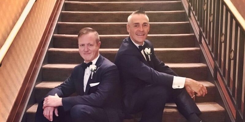 Two men in black tie seated back-to-back on stairway