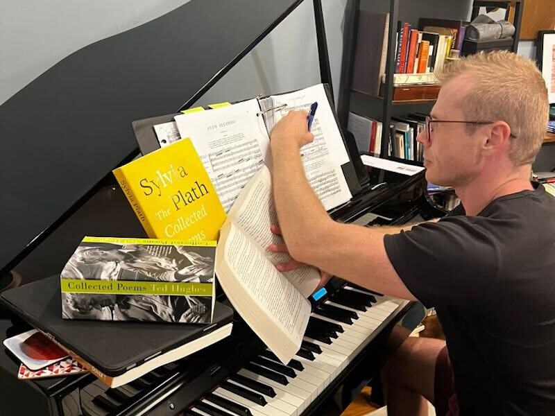 The artistic director Timothy Nelson seated at a piano with books and a score.