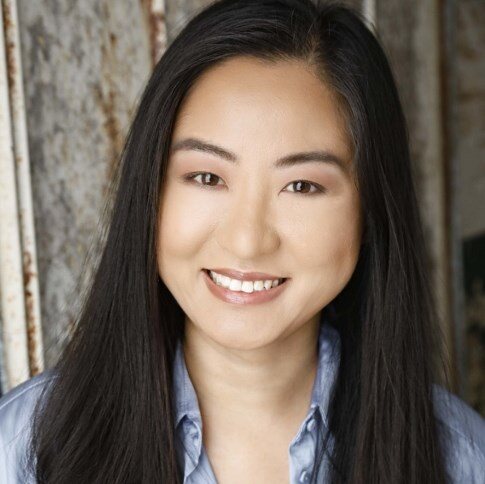 Asian american woman with long black hair and brown eyes smiling and wearing blue dress shirt
